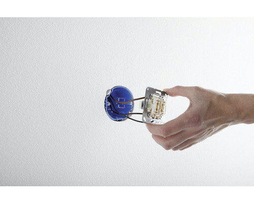 Une main installe un interrupteur dans un boîtier mural.