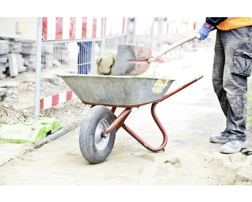 Ouvrier du bâtiment remplissant une brouette avec une pelle sur un chantier