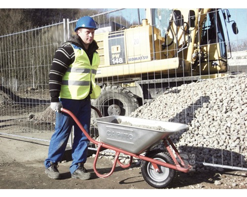 Ouvrier pousse une brouette de ballast devant un engin de chantier