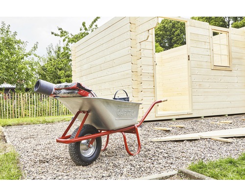 Brouette en métal avec matériaux de construction devant une cabane de jardin en bois en construction