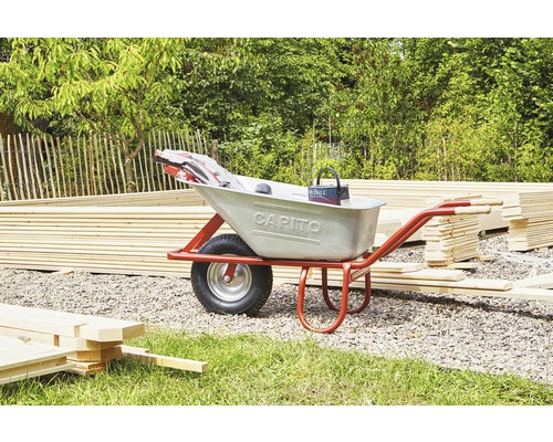 Une brouette avec du matériel de construction et des outils dans un jardin.