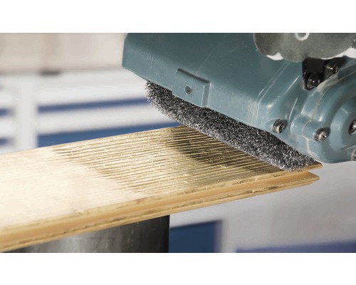 Une brosse métallique travaille une planche de bois.