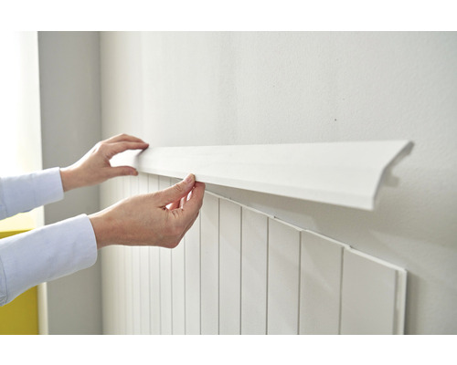 Une personne installe une moulure décorative blanche sur un mur avec des panneaux
