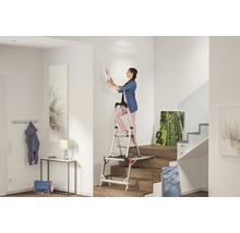 Frau auf einer Podesttreppe in einem hellen Treppenhaus, die ein Bild aufhängt