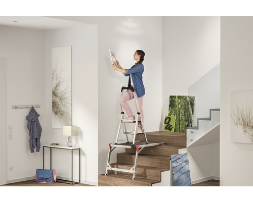 Frau auf einer Podesttreppe in einem hellen Treppenhaus, die ein Bild aufhängt