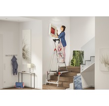 Frau hängt Bild mit einer Treppenleiter im Flur auf