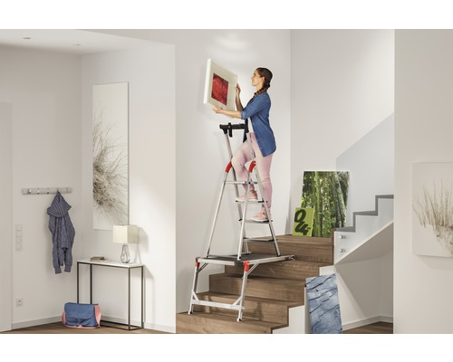 Frau hängt Bild mit einer Treppenleiter im Flur auf