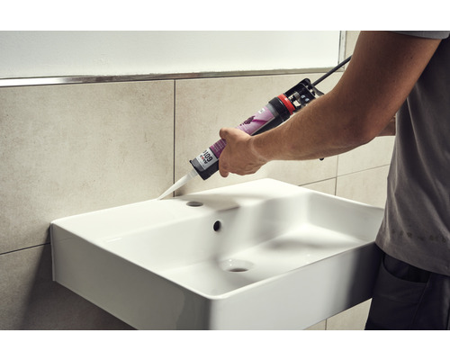 Ein Handwerker dichtet ein Waschbecken mit Silikon ab.