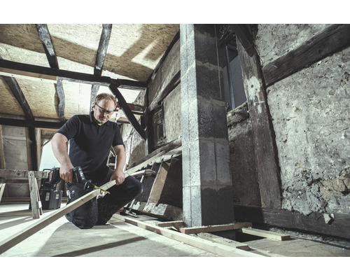 Artisan sciant du bois avec une scie sabre dans une pièce non rénovée.