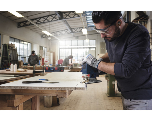 Ein Mann sägt mit einer Stichsäge ein Werkstück in einer Werkstatt.