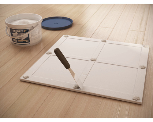 Panneau décoratif avec points de colle, spatule et seau sur plancher en bois