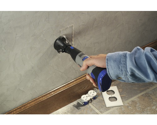 Une personne utilise un outil multifonction pour découper une ouverture dans un mur pour une prise électrique.