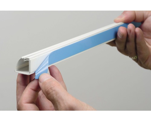 Person entfernt die Schutzfolie von einem selbstklebenden Kabelkanal.