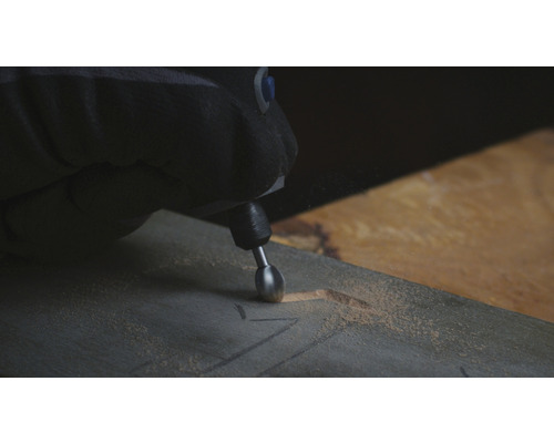 Une personne grave un motif dans une planche de bois avec un outil multifonction.