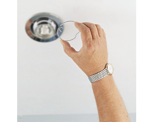 Une main tient un ressort de retenue pour un spot encastrable de plafond.