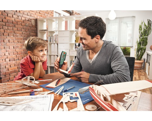 Un père et son fils construisent ensemble un modèle d''avion avec un pistolet à colle sur une table.