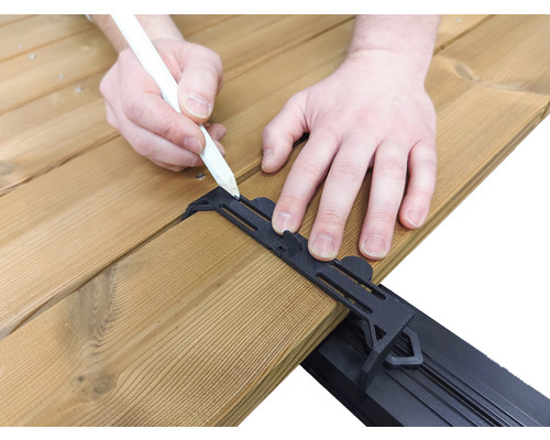 Une personne dessine avec un crayon sur une terrasse en bois avec un support d''écartement noir.