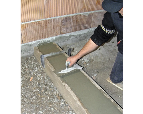 Une personne lisse du béton dans un coffrage en bois avec une truelle.
