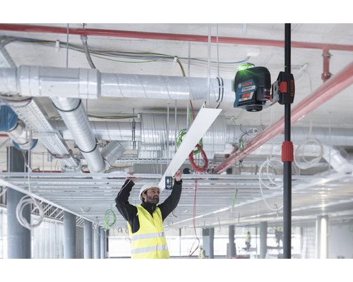 Un ouvrier portant un casque de protection et un gilet de signalisation installe un plafond à l'aide d'un niveau laser de Bosch.