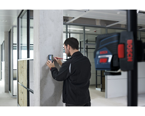 "Un homme utilise un appareil de mesure numérique sur un mur en béton 