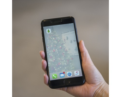 Un téléphone portable est tenu à la main et affiche l''application Hornbach avec un arbre de Noël en arrière-plan.