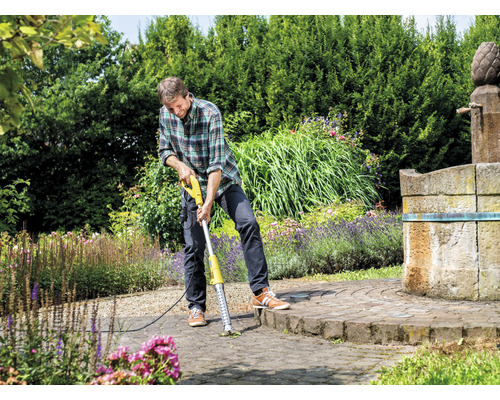 Mann entfernt Unkraut mit einem elektrischen Fugenkratzer auf einer gepflasterten Fläche im Garten.