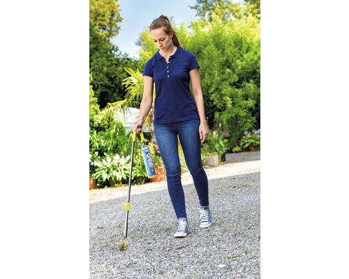 Une femme élimine les mauvaises herbes avec un brûleur à gaz dans le jardin.