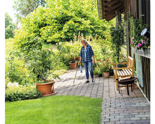 Une femme utilise un désherbant sur des pavés dans le jardin.