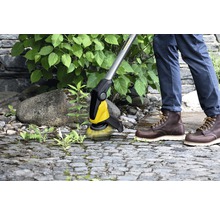 Une personne enlève les mauvaises herbes des pavés avec une brosse Kärcher