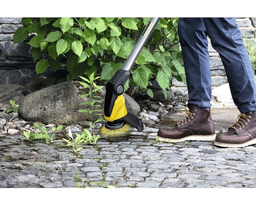 Une personne enlève les mauvaises herbes des pavés avec une brosse Kärcher