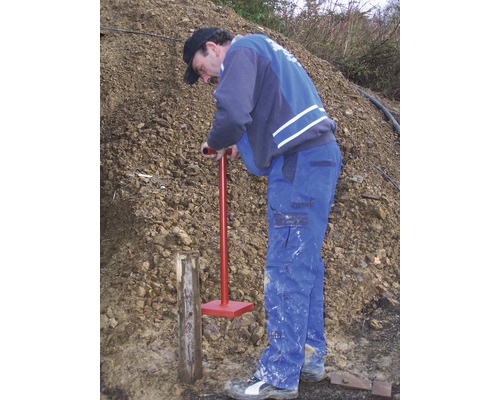 Ein Mann rammt einen Holzpfosten mit einem Erdrammer in den Boden.