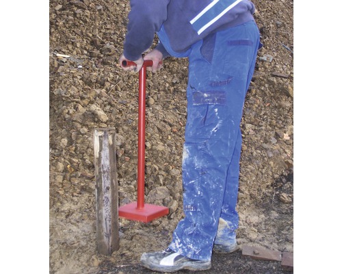 Eine Person rammt einen Holzpfosten mit einem Erdstampfer in den Boden.