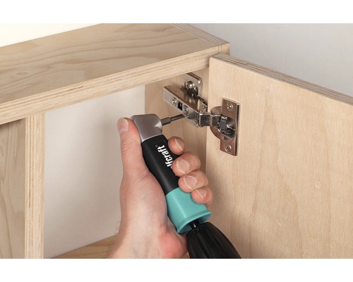 Eine Person befestigt ein Möbelscharnier mit einem Winkelschrauber an einem Holzschrank.