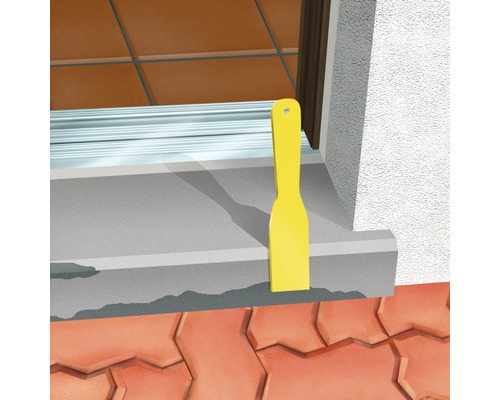 Un lisseur de joints jaune est utilisé pour sceller un rebord de fenêtre.