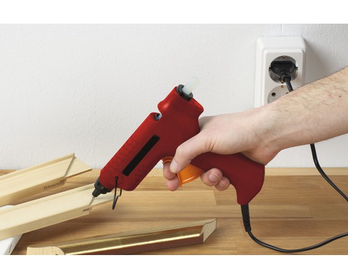 Une main tient un pistolet à colle chaude pour coller un cadre en bois.