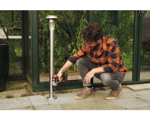 Un homme fixe une lampe solaire avec une visseuse sans fil dans le jardin.