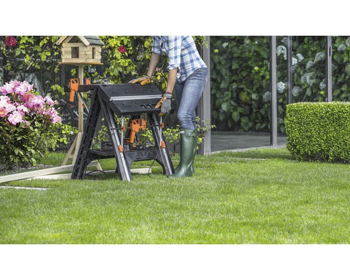 Une femme travaille sur un établi pliant dans le jardin.