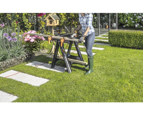 Une femme coupe du bois avec une scie circulaire sur un établi dans le jardin.