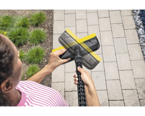 Une femme utilise une buse de nettoyage de surfaces pour nettoyer une surface pavée à l''extérieur.