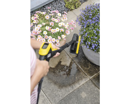 Un opérateur nettoie des dalles en pierre avec une brosse électrique dans le jardin.
