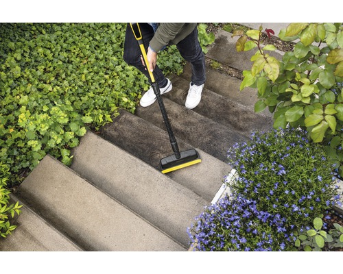 Une personne nettoie un escalier extérieur avec un nettoyeur de surfaces.