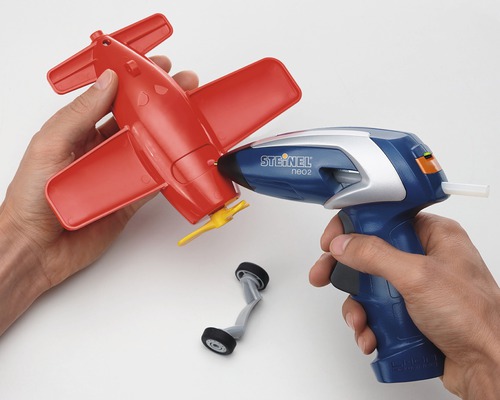 Une personne assemble un avion-jouet rouge avec un pistolet à colle chaude.