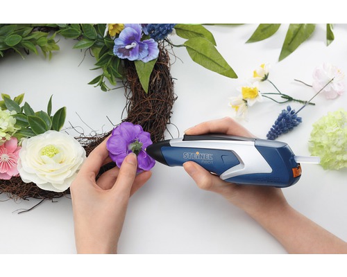 Une personne fixe une fleur à une couronne avec un pistolet à colle chaude.