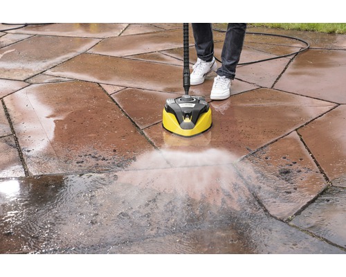 Une personne nettoie des pavés avec un nettoyeur de surfaces Kärcher.
