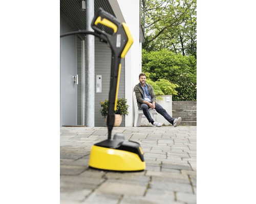 Gelber Flächenreiniger vor einem Haus mit sitzendem Mann