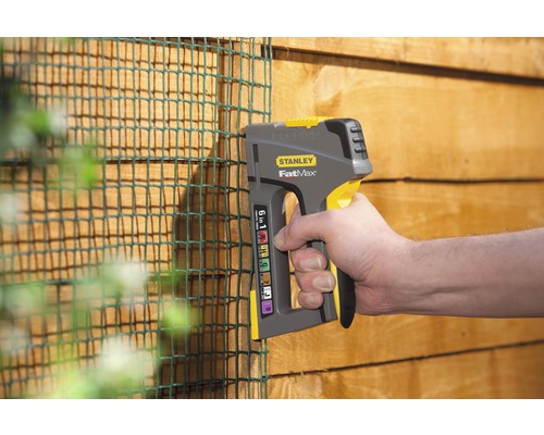 Eine Person befestigt mit einem Tacker ein grünes Netz an einer Holzwand. Stanley FatMax Logo.