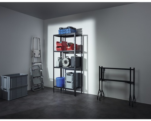 Aufnahme eines Kellers mit einem Regal, das Kisten, Werkzeugkästen, eine Kabeltrommel und einen Eimer enthält, sowie einer Leiter, zwei grauen Klappboxen und einem Tapeziertisch.