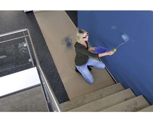 Femme peignant un mur bleu au rouleau, papier de protection sur le sol