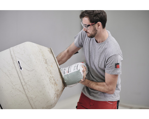 Mann mit Schutzbrille giesst 30 kg Sack Mörtel in einen Betonmischer
