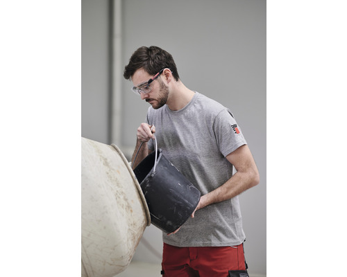 Mann mit Schutzbrille schüttet Inhalt aus einem Eimer in einen Betonmischer